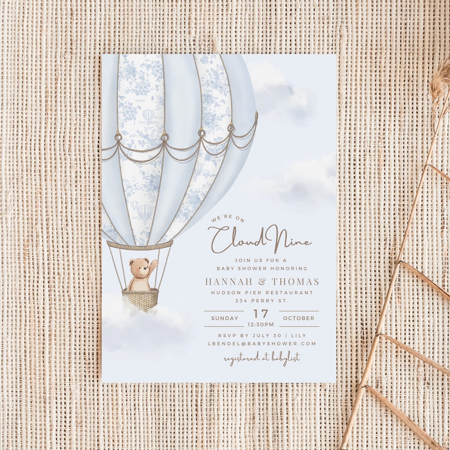Baby shower invitation with hot air balloon and teddy bear design on a textured surface