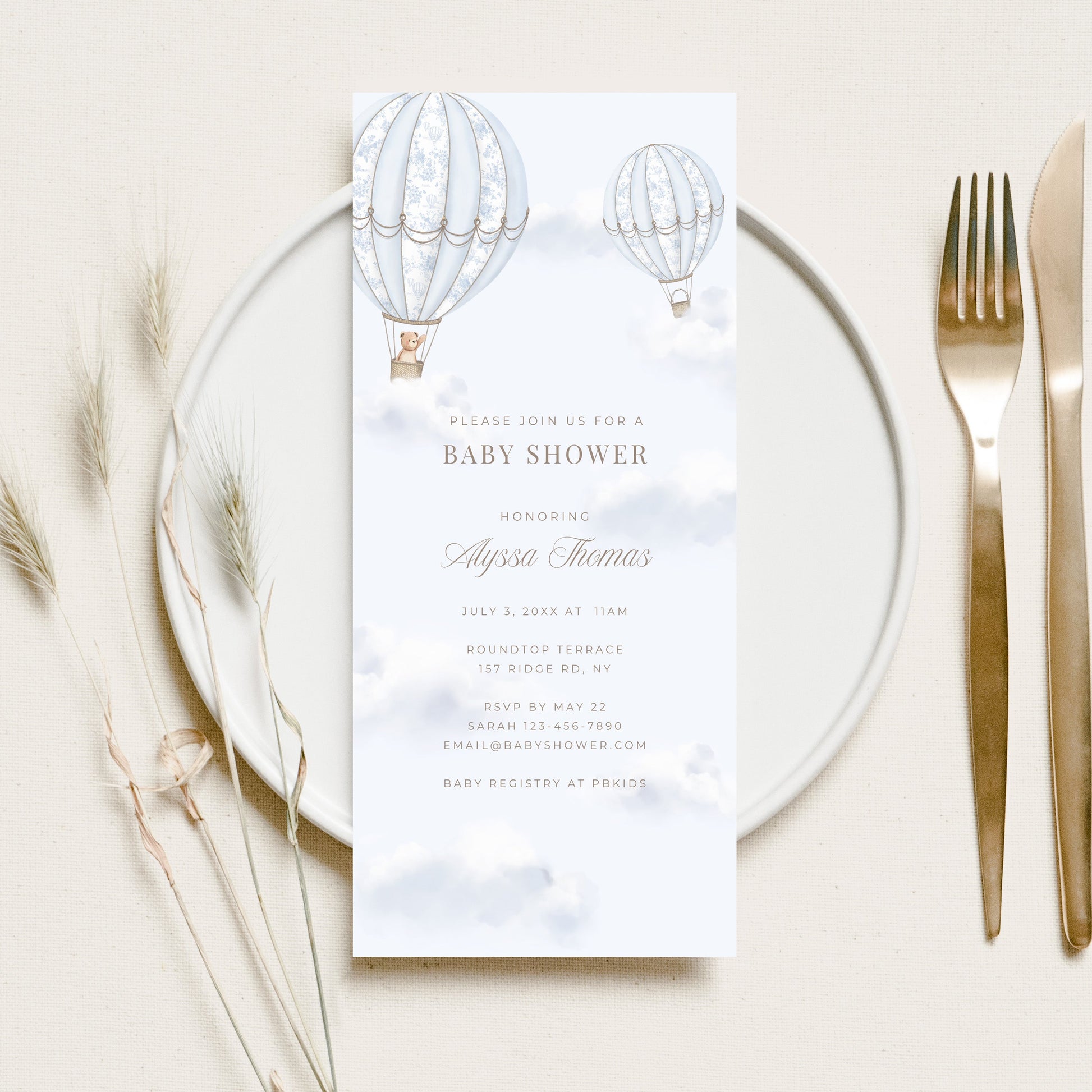 Baby shower invitation card on a glass plate with cutlery and dried flowers.