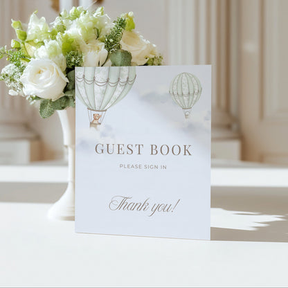 Guest book Table Sign with hot air balloon design next to a floral arrangement on a table.