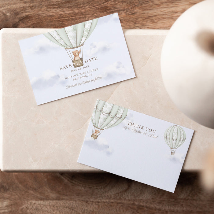 Two cards with hot air balloon designs on a wooden surface with a vase.