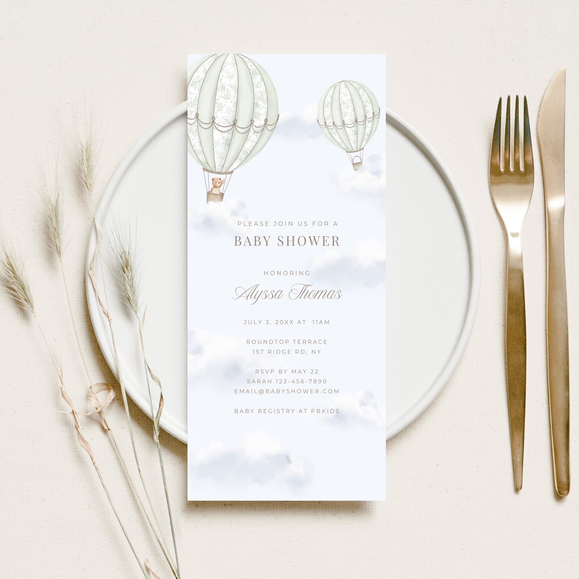 Baby shower invitation card on a glass plate with cutlery and decorative elements.
