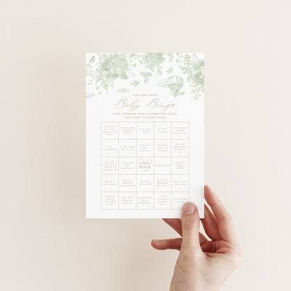Hand holding a Baby Bingo Game Card with a sage green floral pattern against a neutral background