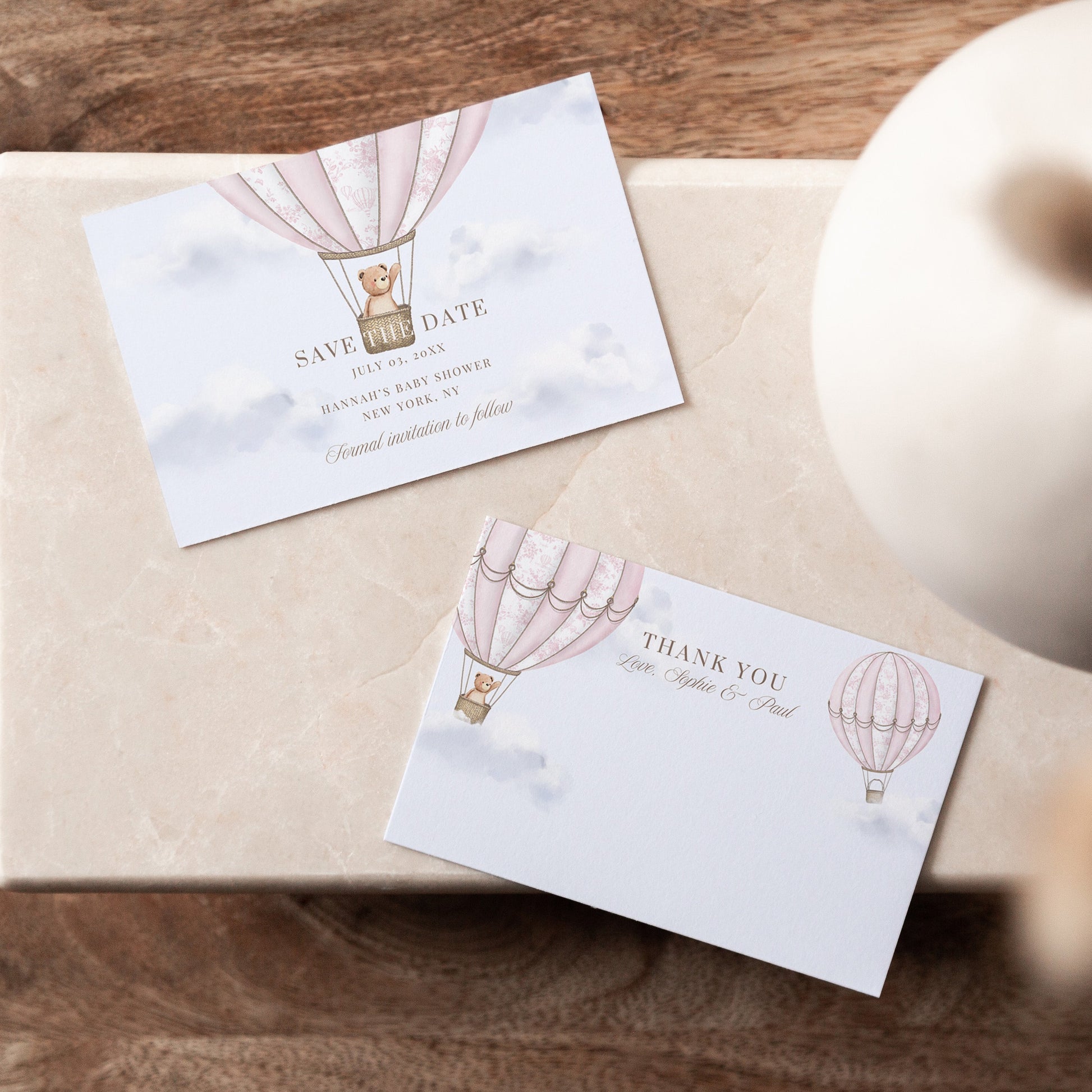 Two cards with hot air balloon design on a wooden surface with a vase.
