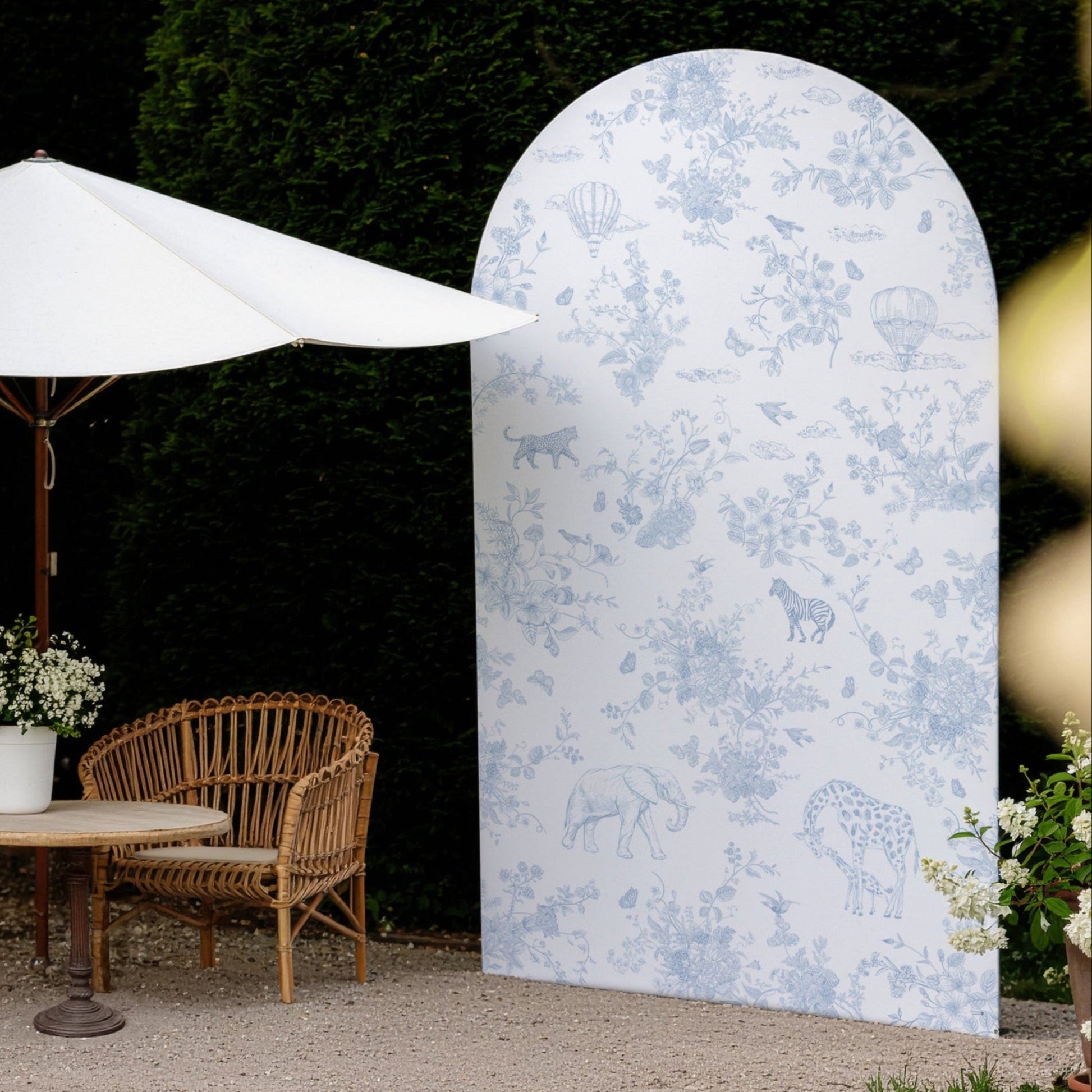 Decorative arch backdrop with animal pattern in a garden setting with furniture and umbrella
