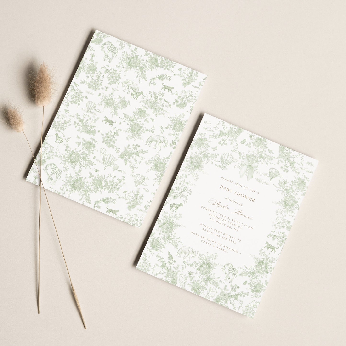 Two floral patterned baby shower invitation cards on a beige surface with dried grasses.
