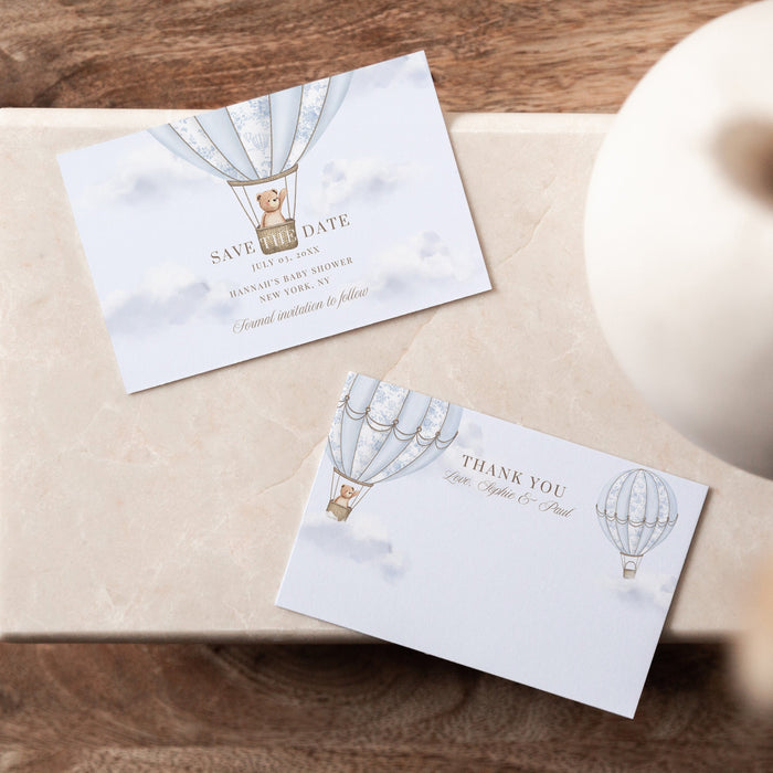 Two cards with hot air balloon designs on a wooden surface with a vase.